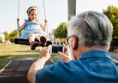 A grandpa pushing his granddaughter on a swing set while on a day out together at the park.